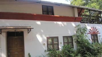 A two-story building with a white facade, a wooden door, and windows with metal grilles.