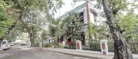 A two-story building with a red and white facade, surrounded by lush greenery and palm trees.