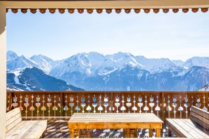 Terraza de madera con banco y mesa, con vistas a montañas nevadas.