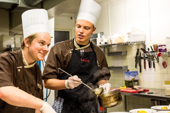 Dos cocineros en una cocina, uno removiendo una olla.