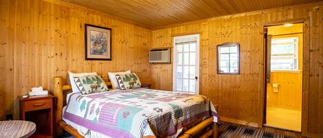 A wooden-paneled bedroom with a bed, bedside table, and a door leading to another room.