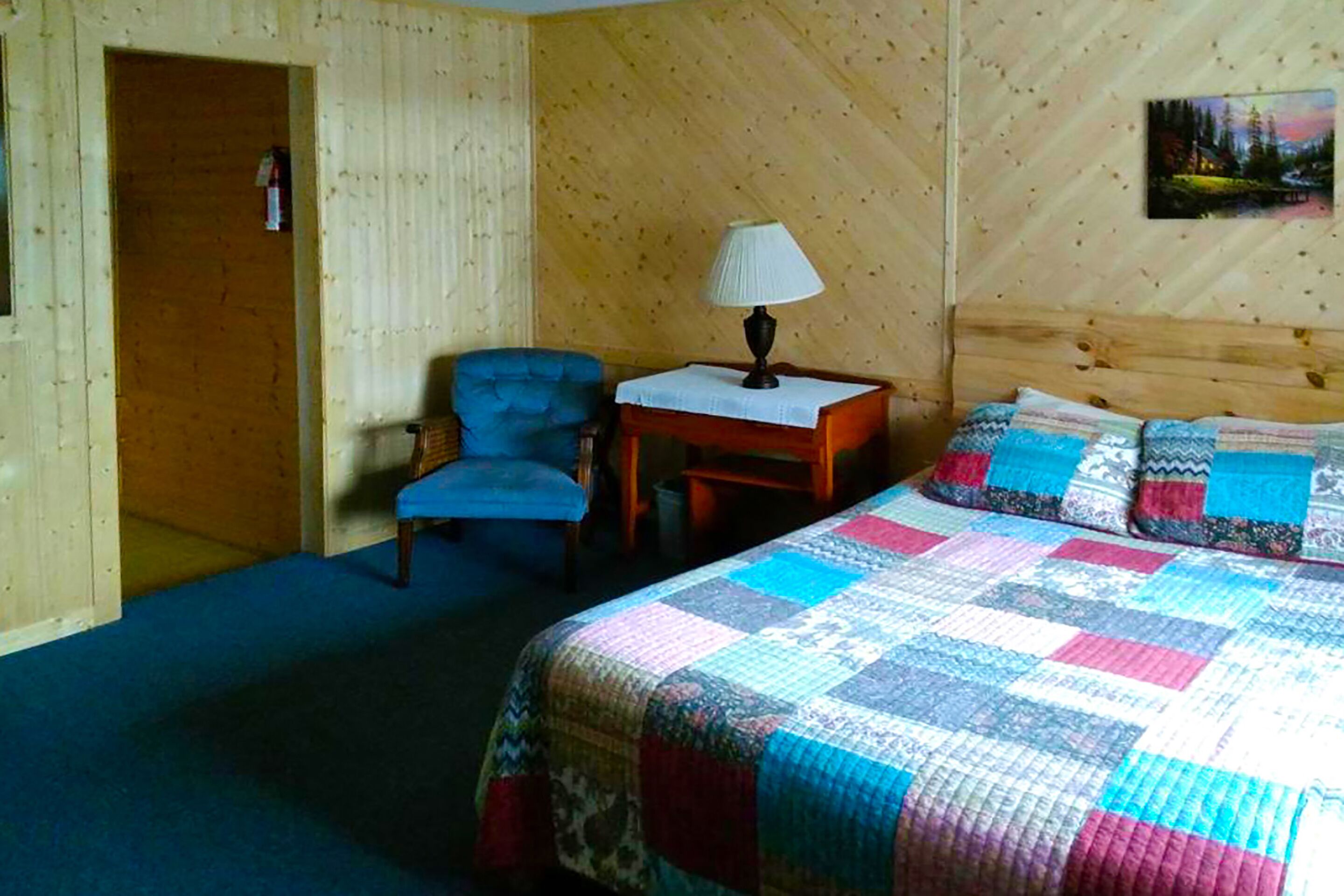Ett rum med en säng, en stol, ett bord med en lampa och en tavla på väggen.