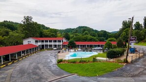 A hotel with a swimming pool, covered parking, and a red-roofed building.