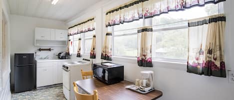 Una cocina compacta con armarios blancos, un refrigerador negro, un microondas, una cafetera y una mesa de madera.