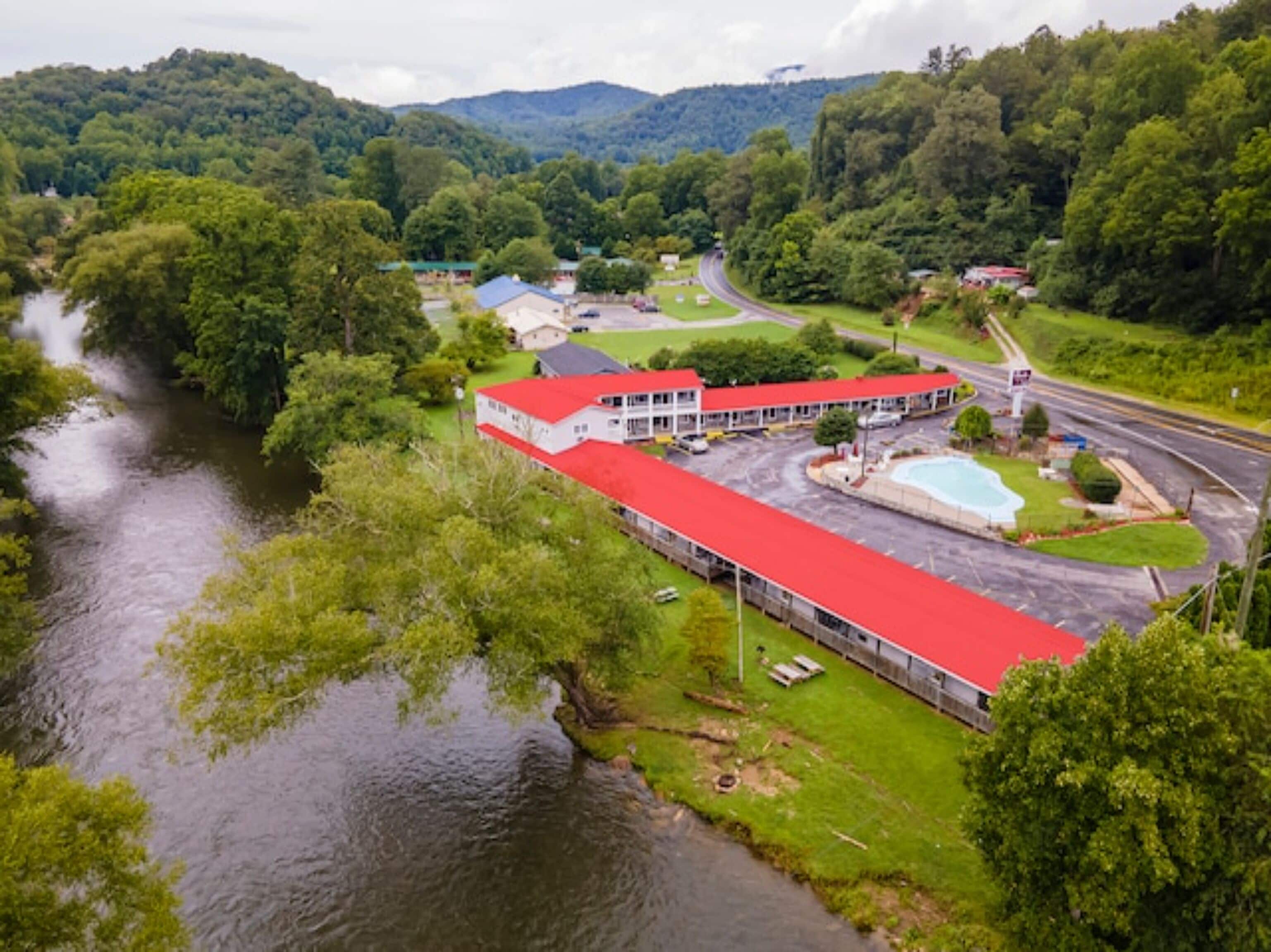 A hotel with a red roof, a swimming pool, and a view of a river.