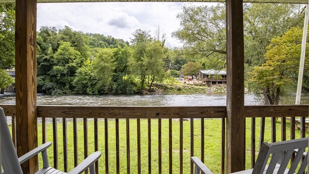 A wooden deck with chairs overlooking a river, surrounded by lush greenery and trees.