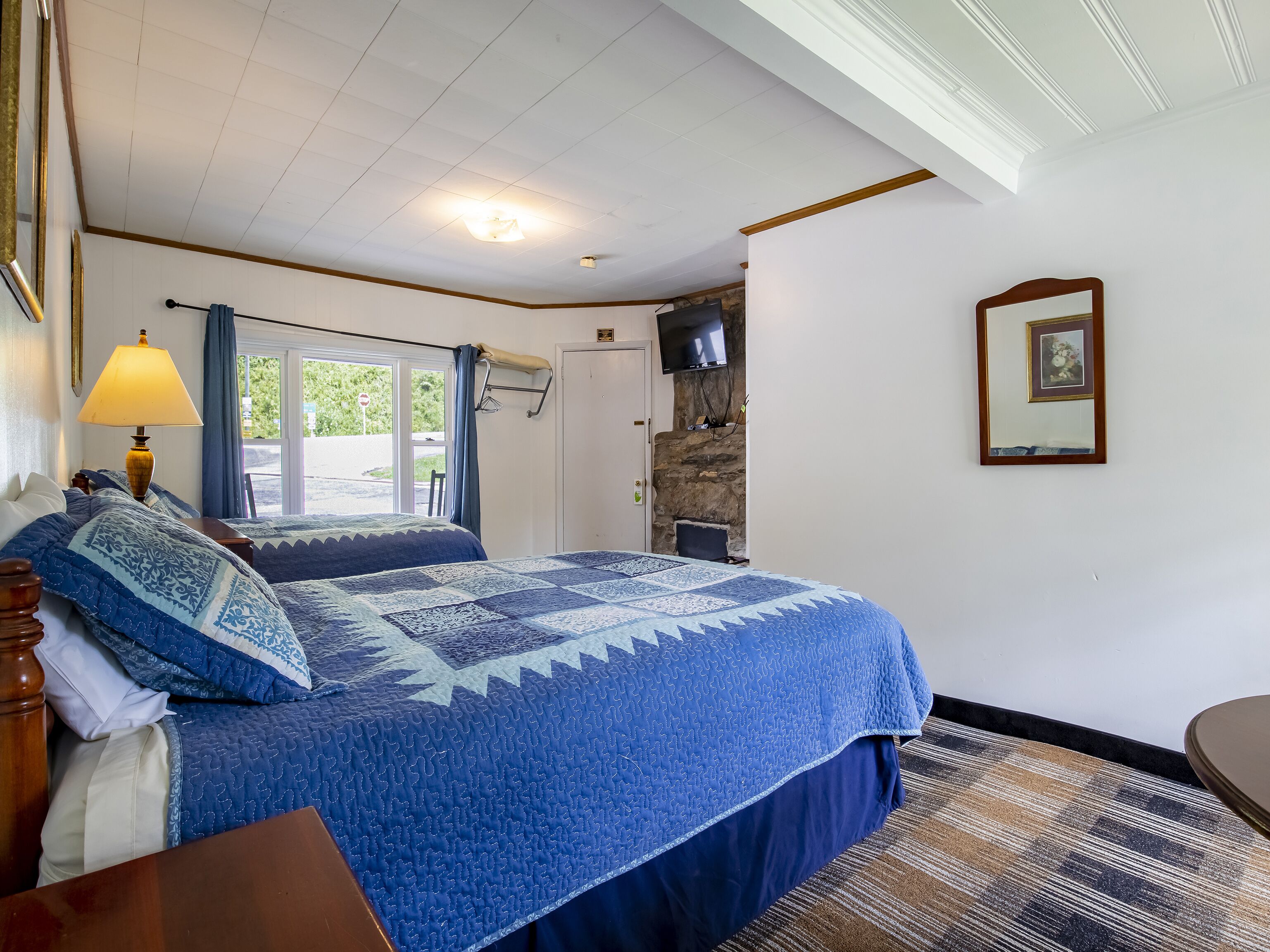 A bedroom with a large bed, a window, a TV, and a stone wall.