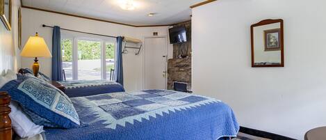 A bedroom with a large bed, a window, a TV, and a stone wall.