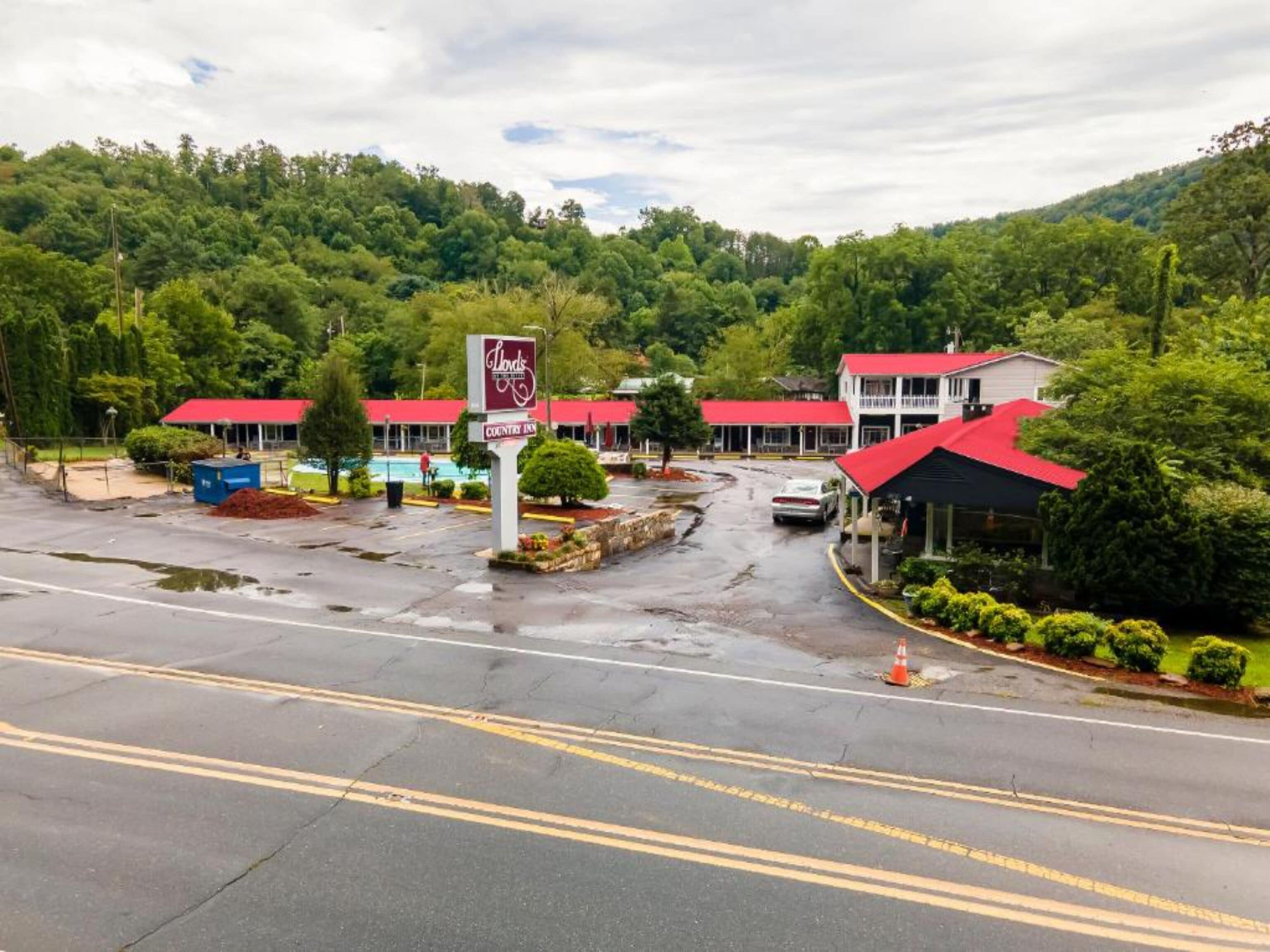 A Country Inn with a red roof and a signboard, surrounded by lush greenery and a parking lot.