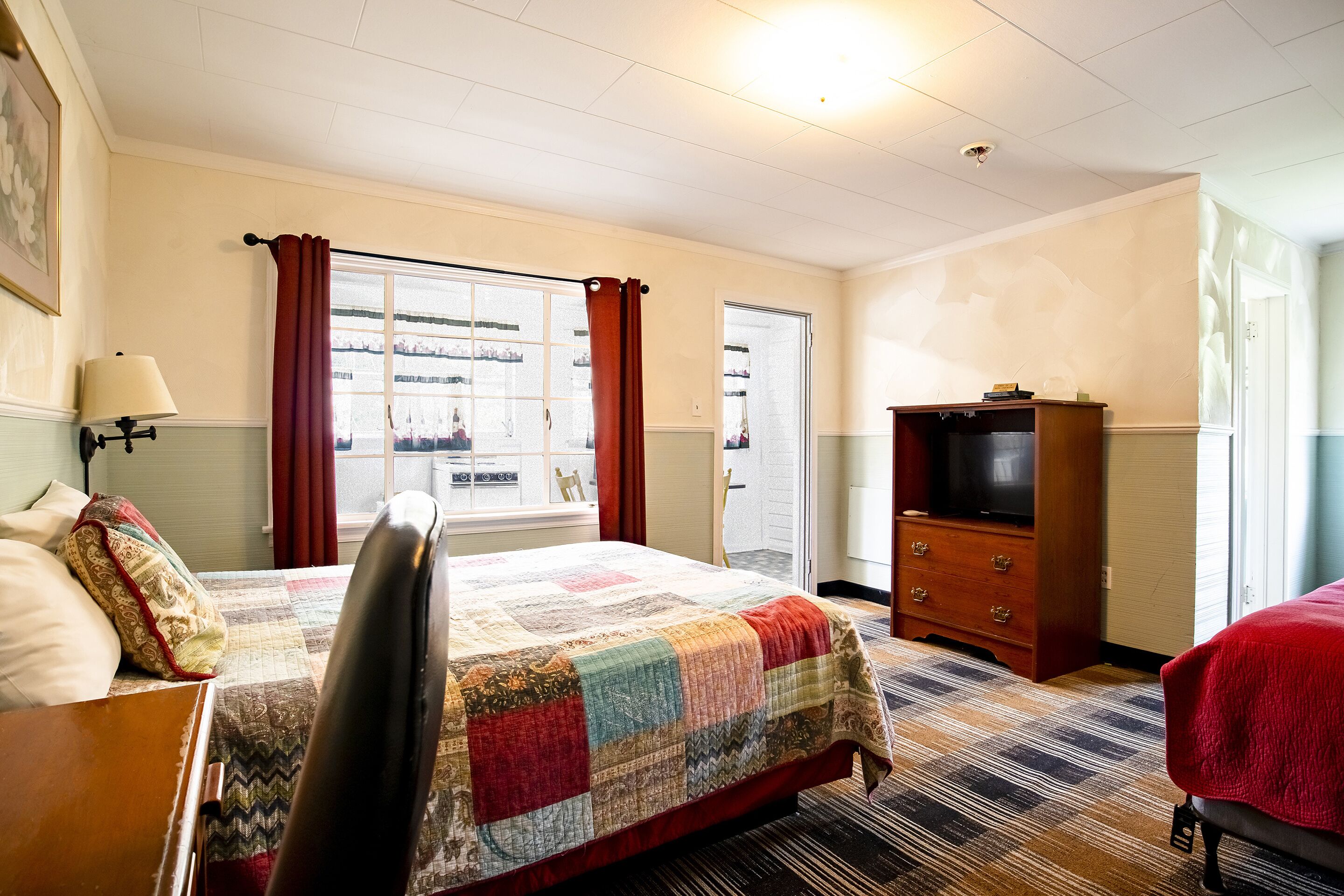 A hotel room with a large bed, a wooden dresser, a television, and a window with curtains.