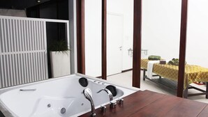 Un baño moderno con una bañera grande, un tocador de madera y vistas a un balcón con cama y mesa.