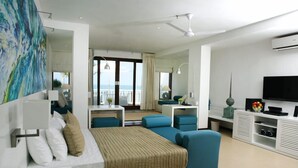 Una habitación de hotel moderna con cama, zona de estar, televisor y balcón con vistas.