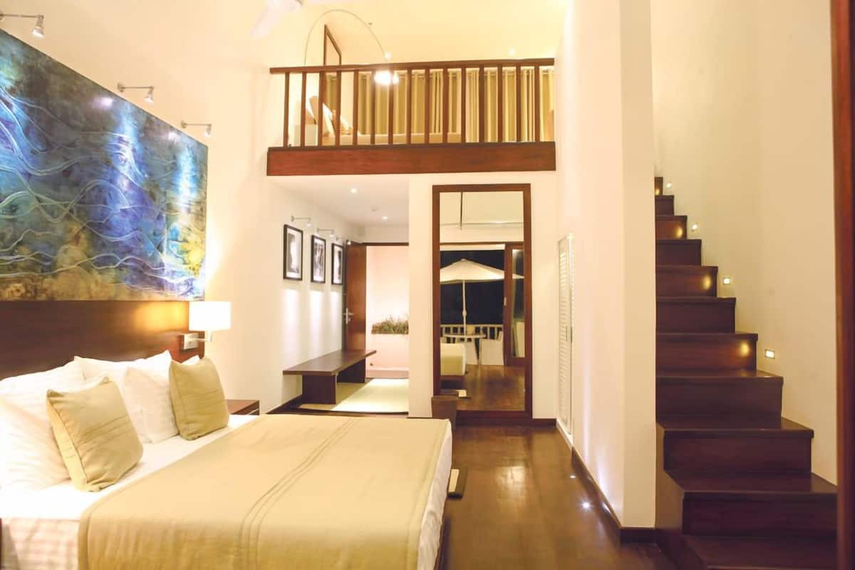 Quarto de hotel com uma cama grande, escada de madeira e vista para a varanda.