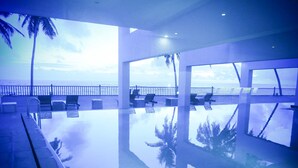 Una piscina infinita con vista al océano, sillas de descanso y palmeras.