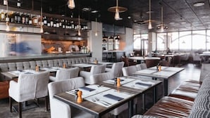 Restaurante moderno com mesas altas, cabines, luminárias pendentes e um bar com prateleiras cheias de garrafas.