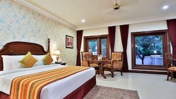 Una habitación de hotel con una cama grande, una zona de estar con una mesa y sillas, un ventilador de techo y una ventana con vistas al exterior.