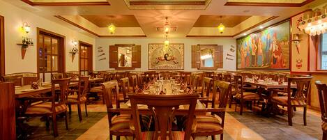 A spacious dining area with multiple tables and chairs, wooden ceiling, and decorative lighting fixtures.