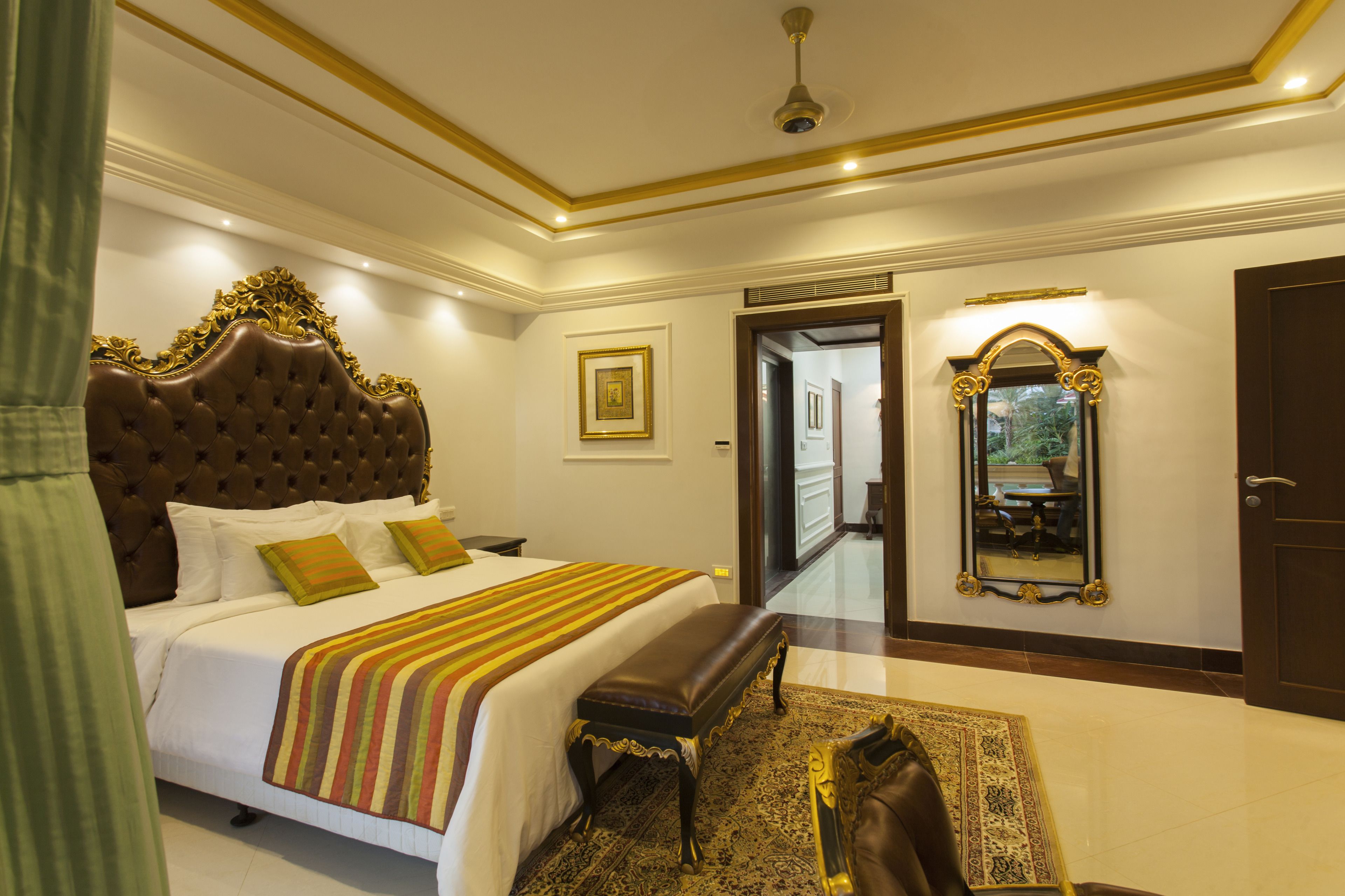 A bedroom with a large bed, a bench, a mirror, and a door leading to another room.