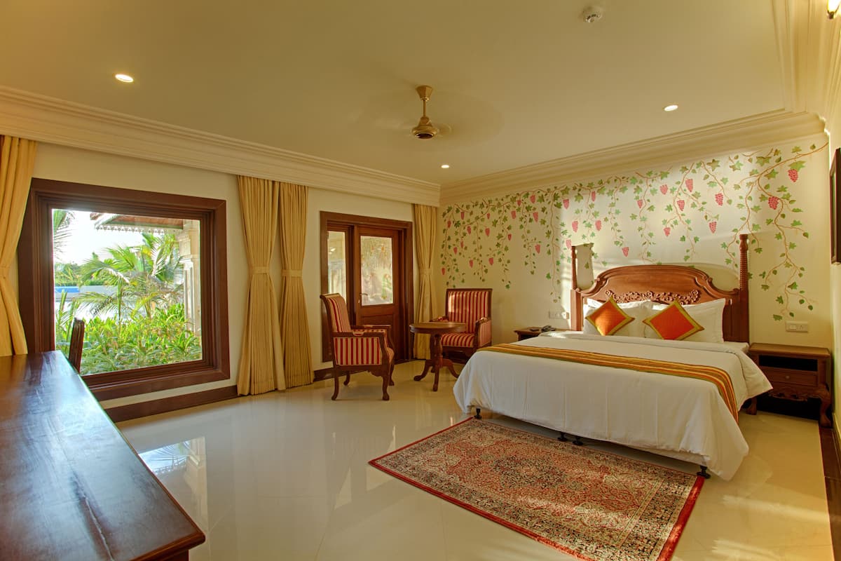 Une chambre d’hôtel avec un grand lit, deux fauteuils, une petite table et une vue sur la verdure par la fenêtre.