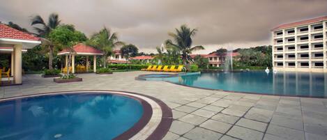 Um resort com várias piscinas, áreas de estar cobertas e um edifício grande com varandas.