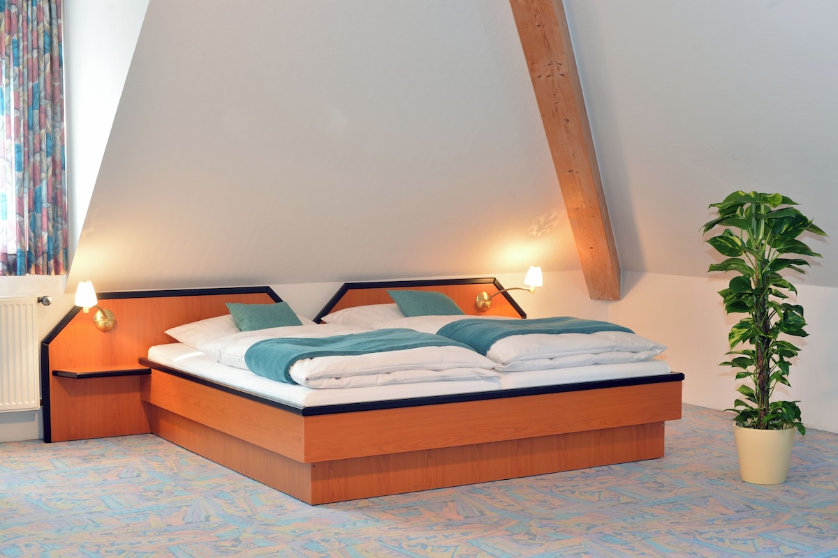 Ein Schlafzimmer mit einem hölzernen Bett, zwei Nachttischlampen, einem Blumentopf und einem Fenster mit Vorhängen.