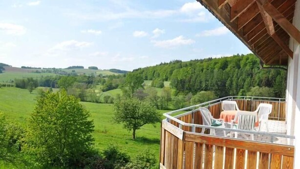 Ein Balkon mit Blick auf eine grüne Landschaft und einer Holzterrasse.