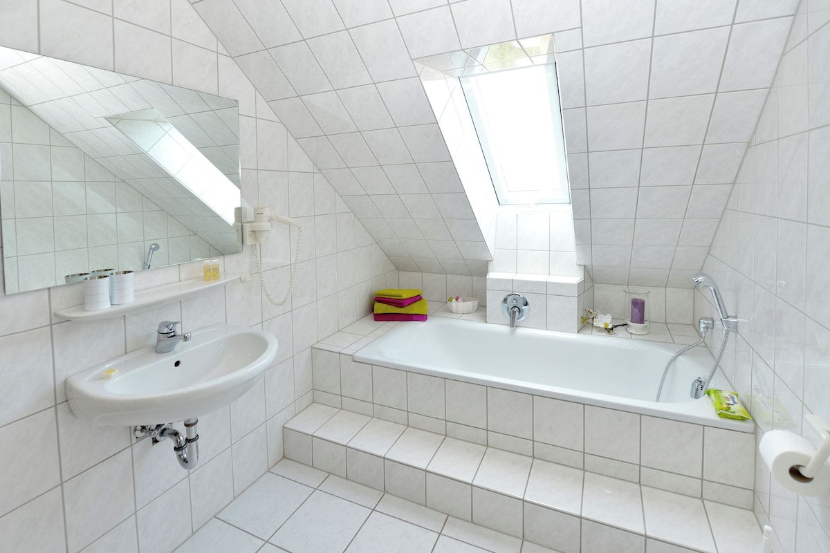 Ein modernes Badezimmer mit großem Spiegel, Waschbecken, Badewanne und einem Fenster für natürliches Licht.
