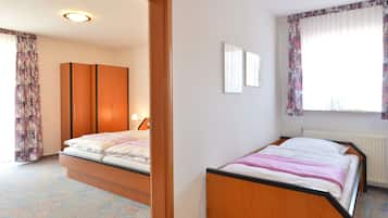 Een slaapkamer met een bed, een kast, een radiator en een raam met gordijnen.