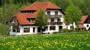 Ein zweistöckiges Gebäude mit rotem Ziegeldach, Balkonen und einem Garten mit gelben Blumen.
