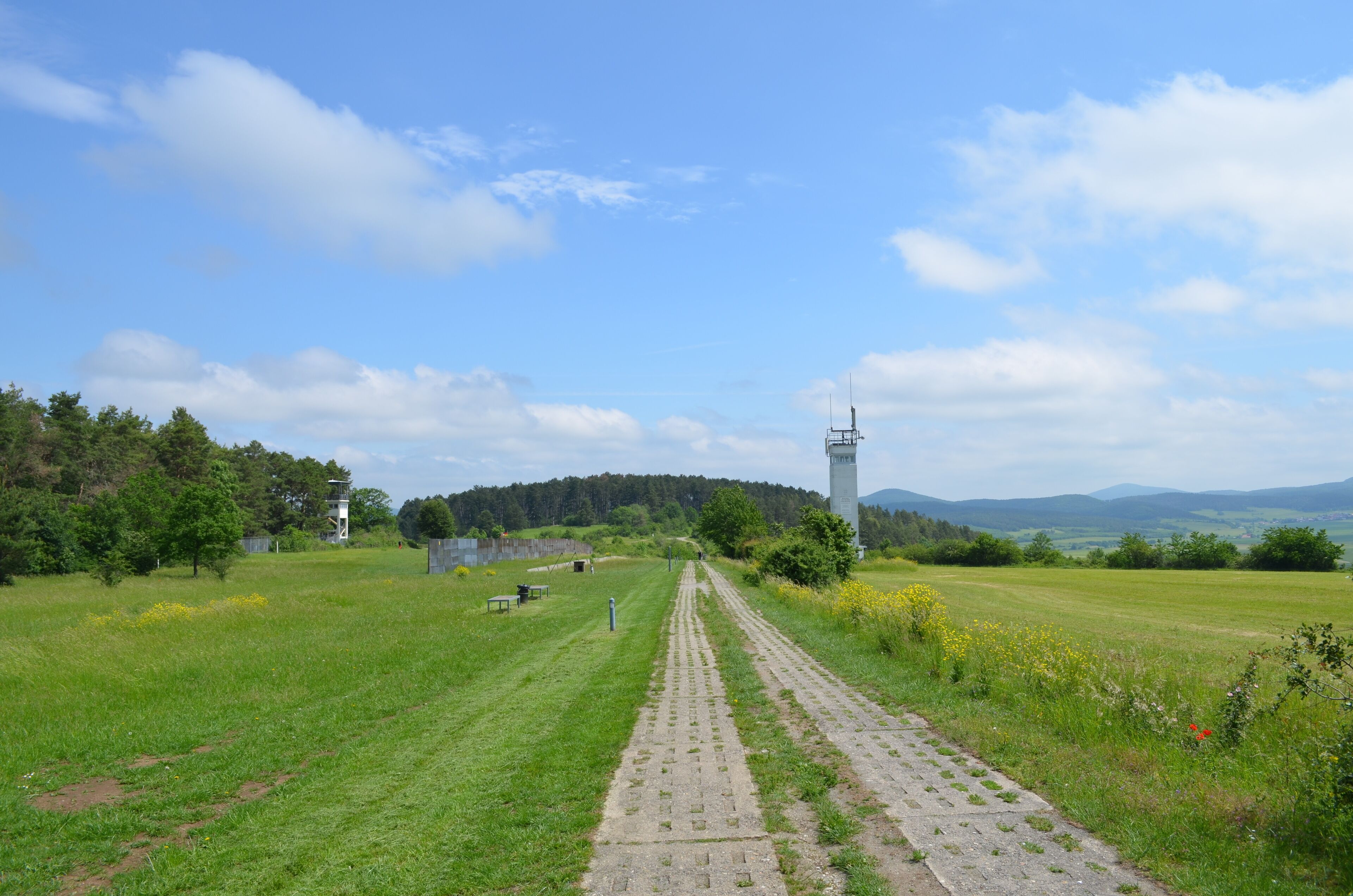 A paved pathway leading through a grassy field with a tower structure in the distance.