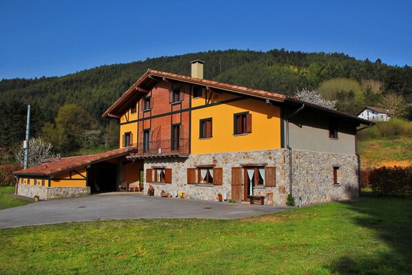 A two-story house with a stone foundation and a yellow facade, featuring a balcony and a garage entrance.