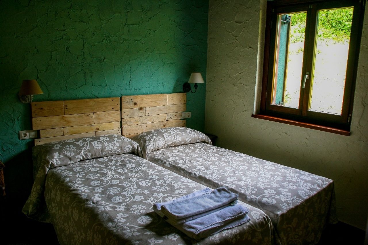 A room with two beds, a window with a view, a lamp, and a wall lamp.