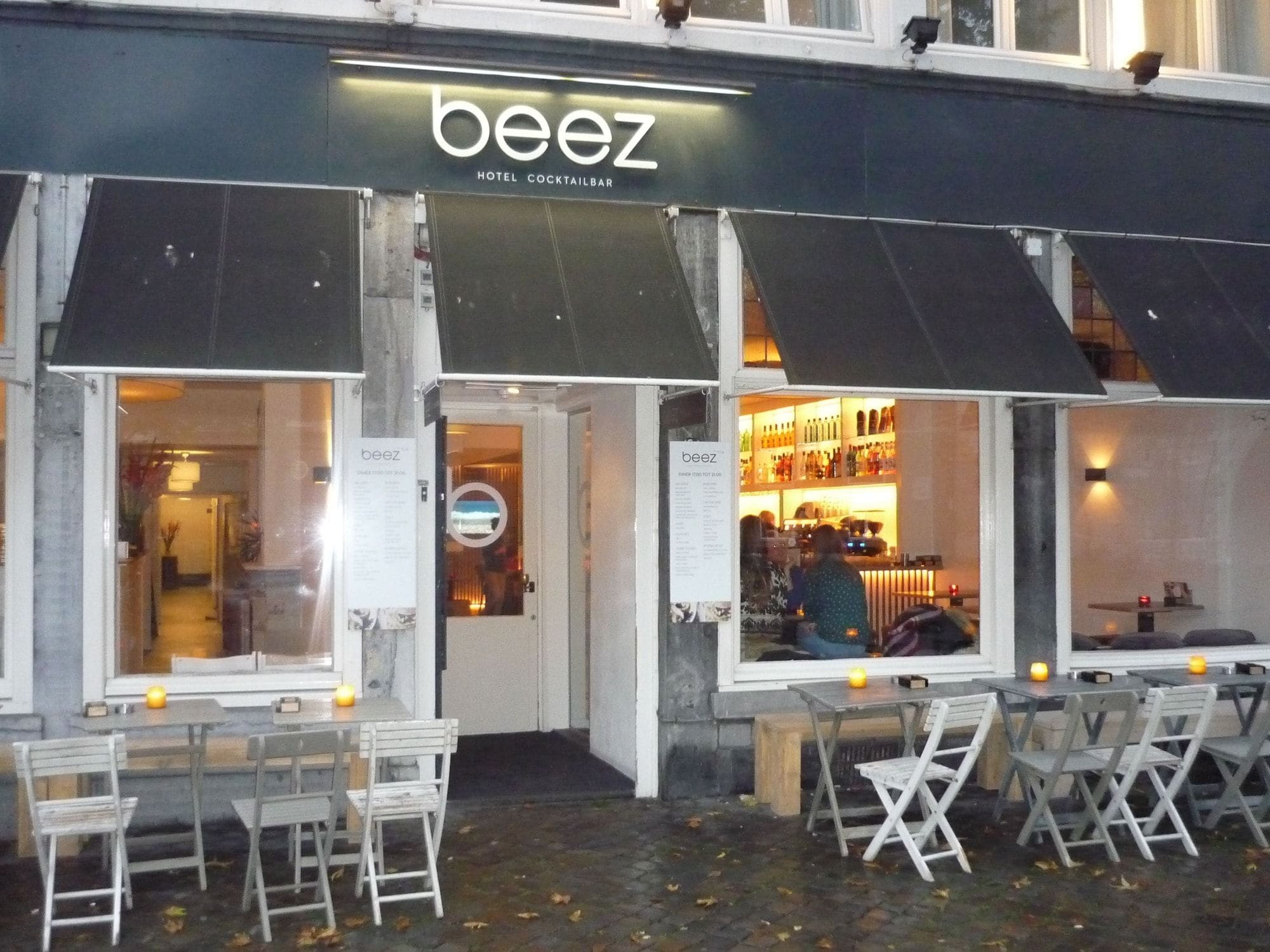 Un área de estar al aire libre con mesas y sillas frente a un edificio con un letrero que dice 'beez'.