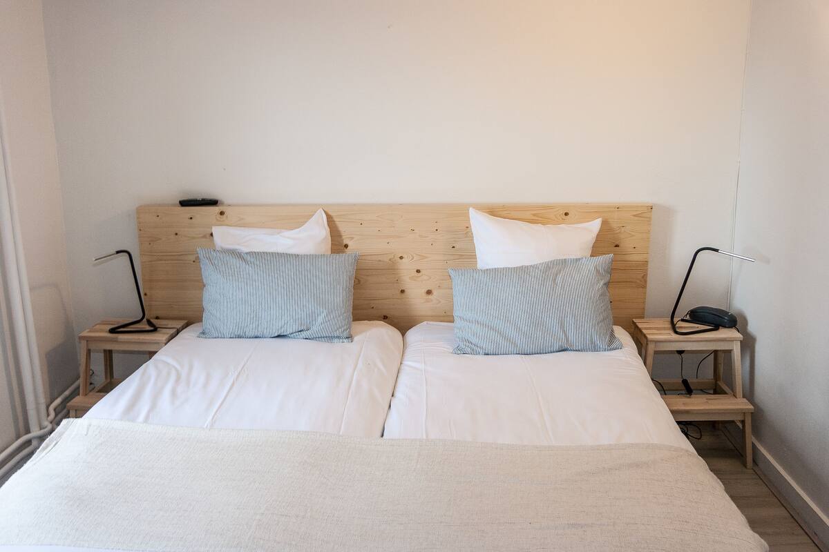 A double bed with white bedding and striped pillows, two bedside tables with lamps, and a wooden headboard.