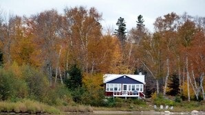 A cabin by a lake surrounded by autumn-colored trees. - Bruce Bay Cottages & Lighthouse (Bruce Mines)