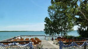 An outdoor seating area with wooden chairs and tables, a white lattice fence, and a view of a body of water. - Bruce Bay Cottages & Lighthouse (Bruce Mines)