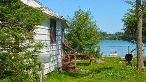 A rustic cabin with a wooden deck and a view of a lake. - Bruce Bay Cottages & Lighthouse (Bruce Mines)