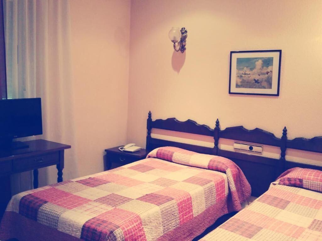 Habitació d'hotel amb dos llits, televisió, taula de nit, làmpada i un quadre al mur.