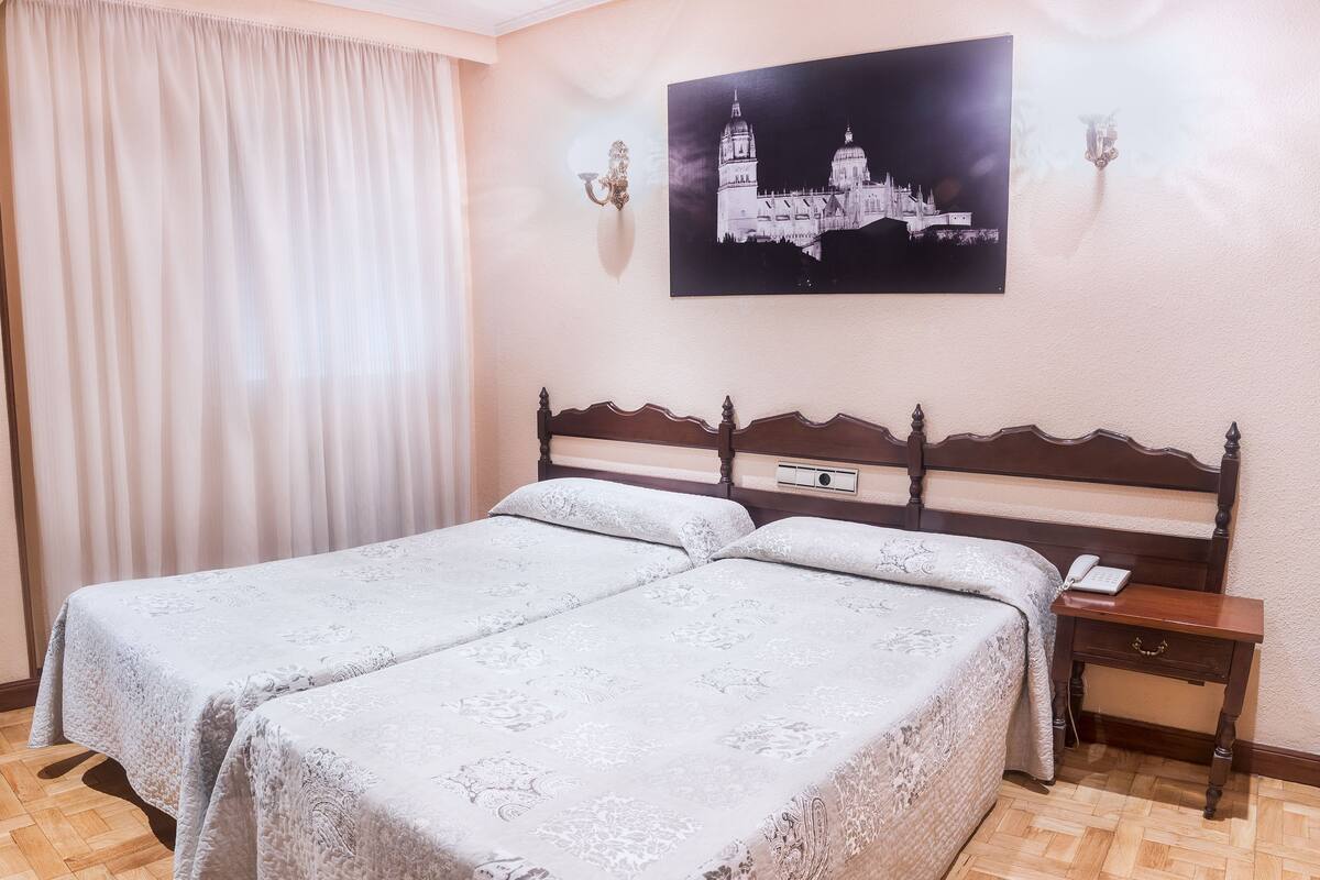 A double bed with a wooden headboard, a nightstand with a phone, and a wall-mounted picture of a cathedral.