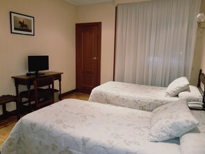 Une chambre d’hôtel avec deux lits, un bureau avec un ordinateur, une porte et une fenêtre avec des rideaux.