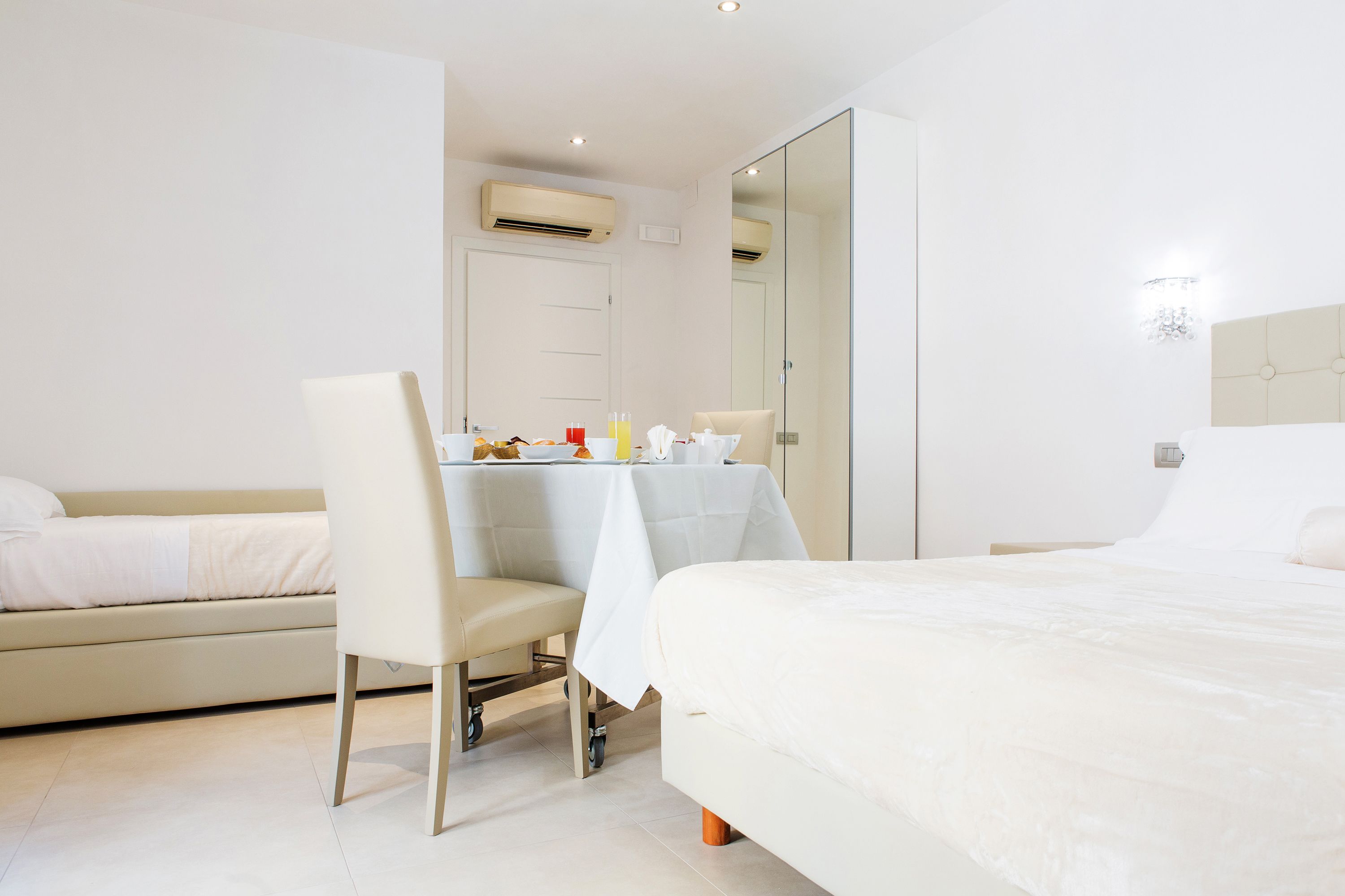 A modern hotel room with a bed, a sofa, a dining table, and a chair.