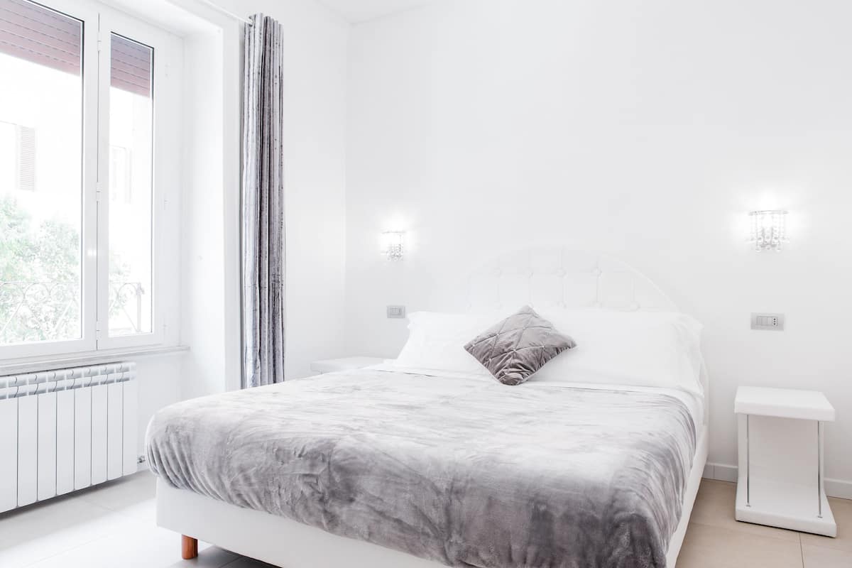 A modern bedroom with a large bed, white walls, and a window with curtains.