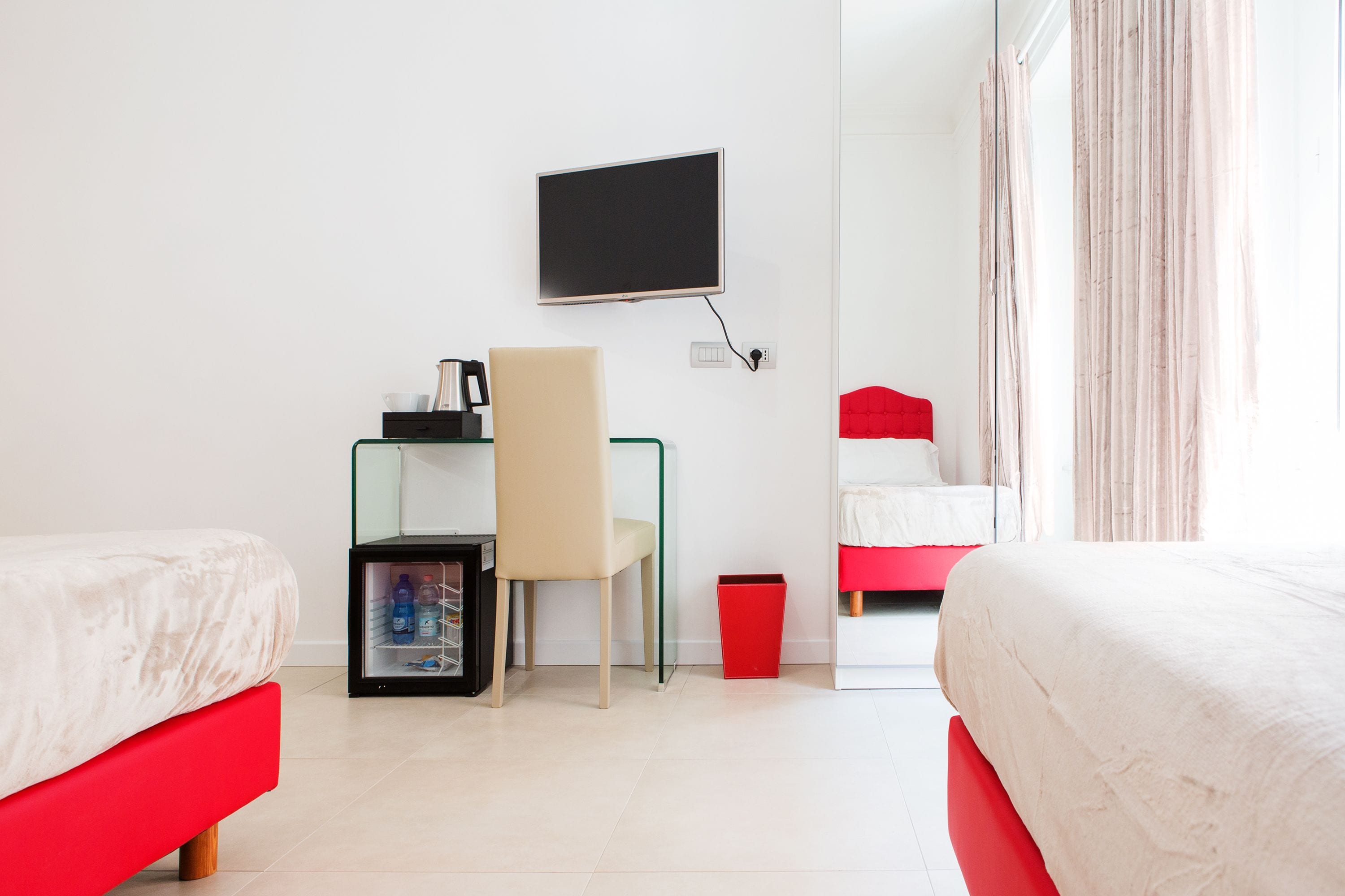 Una camera d'albergo con due letti, una scrivania con una sedia, una TV a parete e un cestino.