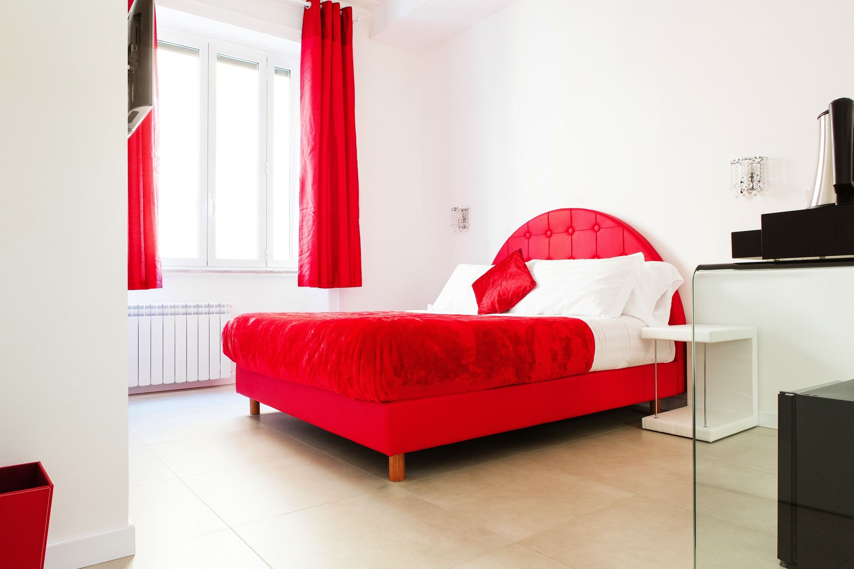 A modern bedroom with a red bed, white walls, and a glass cabinet.