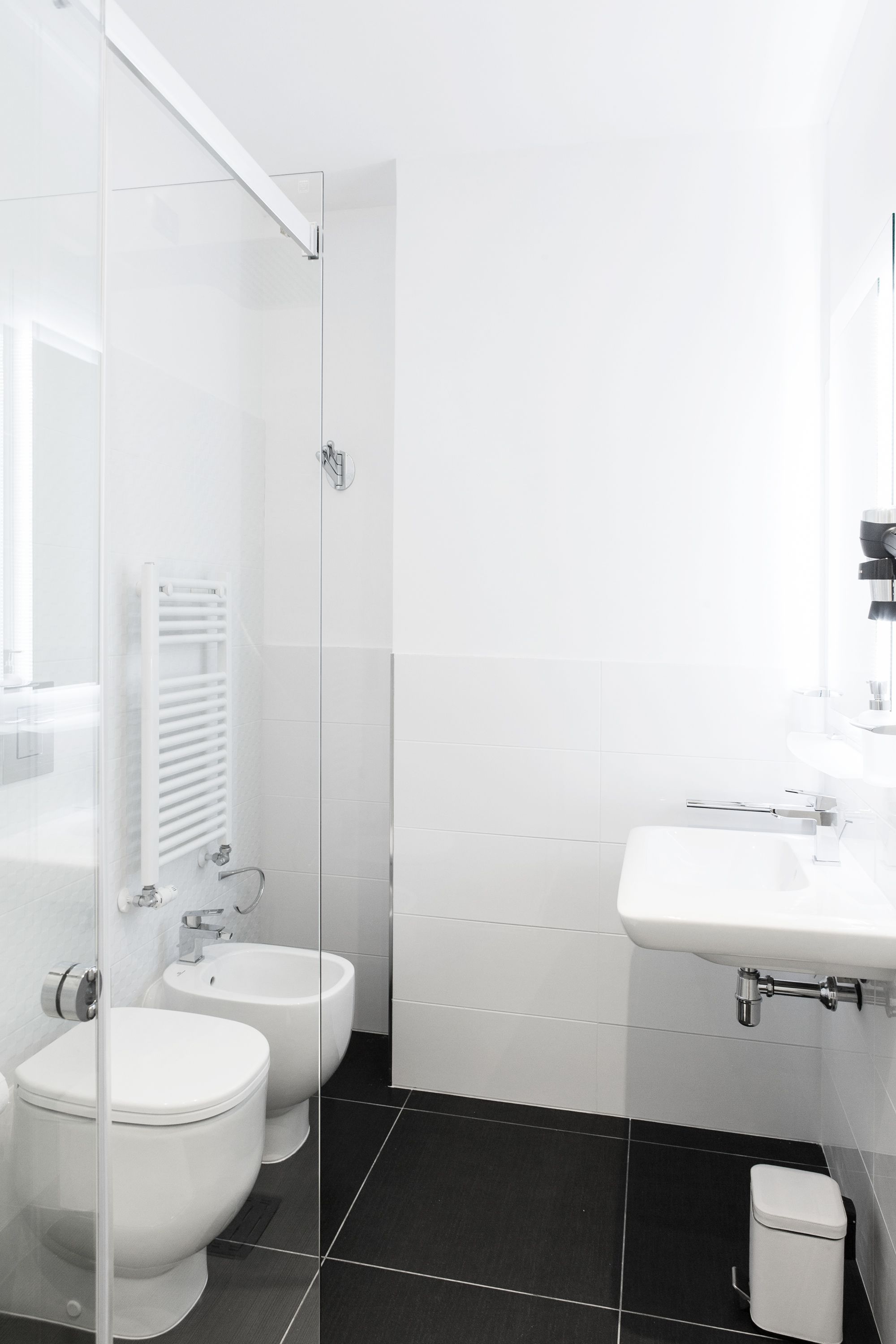 A modern bathroom with a glass shower enclosure, a white sink, and two toilets.