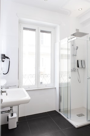 A modern bathroom with a glass shower enclosure, a white sink, and a window with a balcony view. - Vatican Grand Suite (Rome)