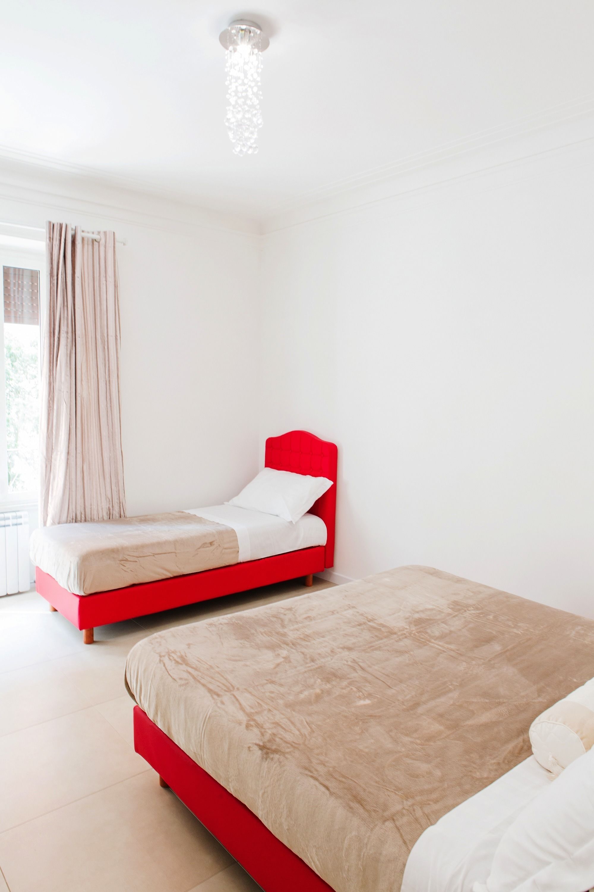 A bedroom with a red bed and a smaller bed with a white headboard.