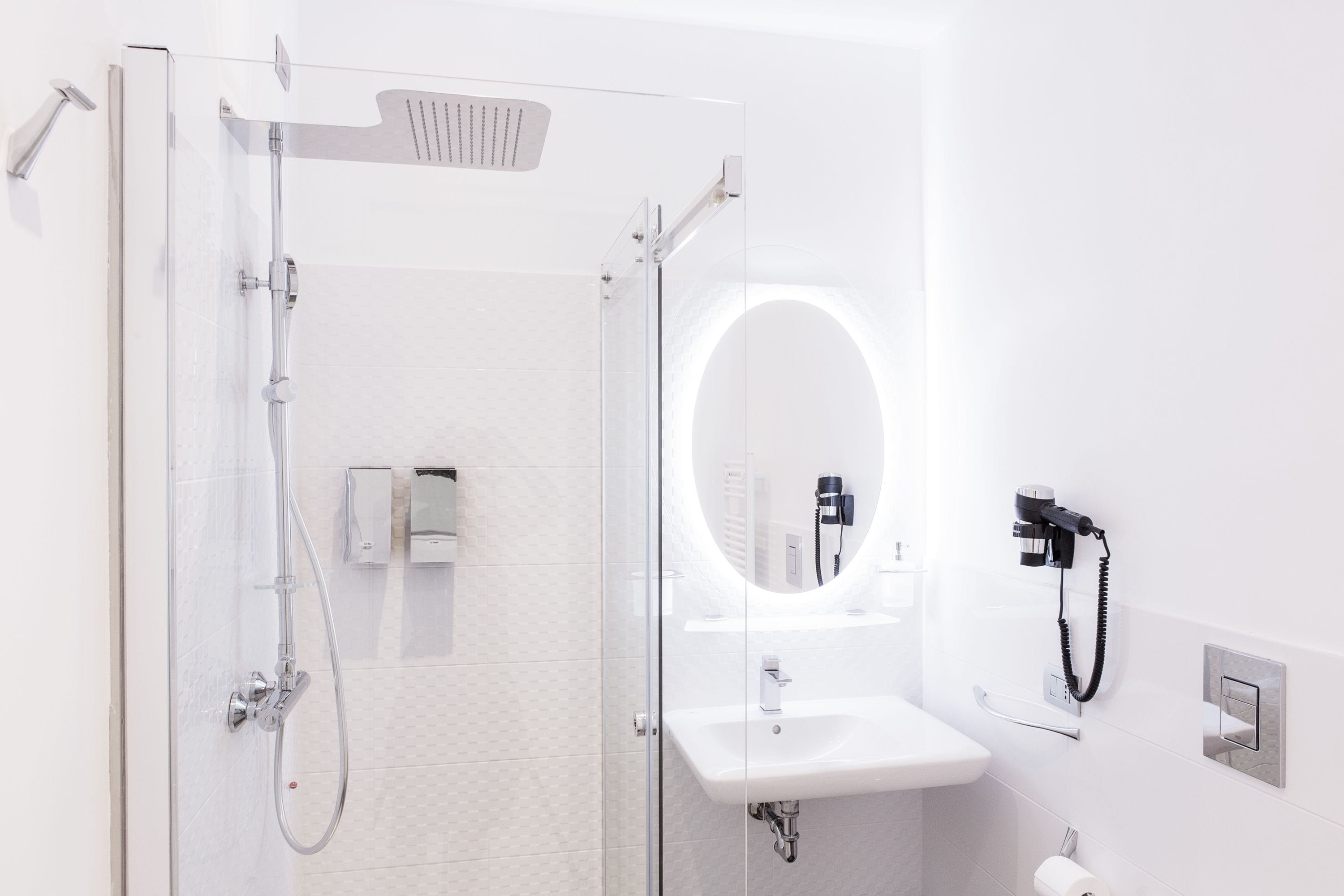 A modern bathroom with a glass-enclosed shower, a sink with a mirror, and a hairdryer on the wall.