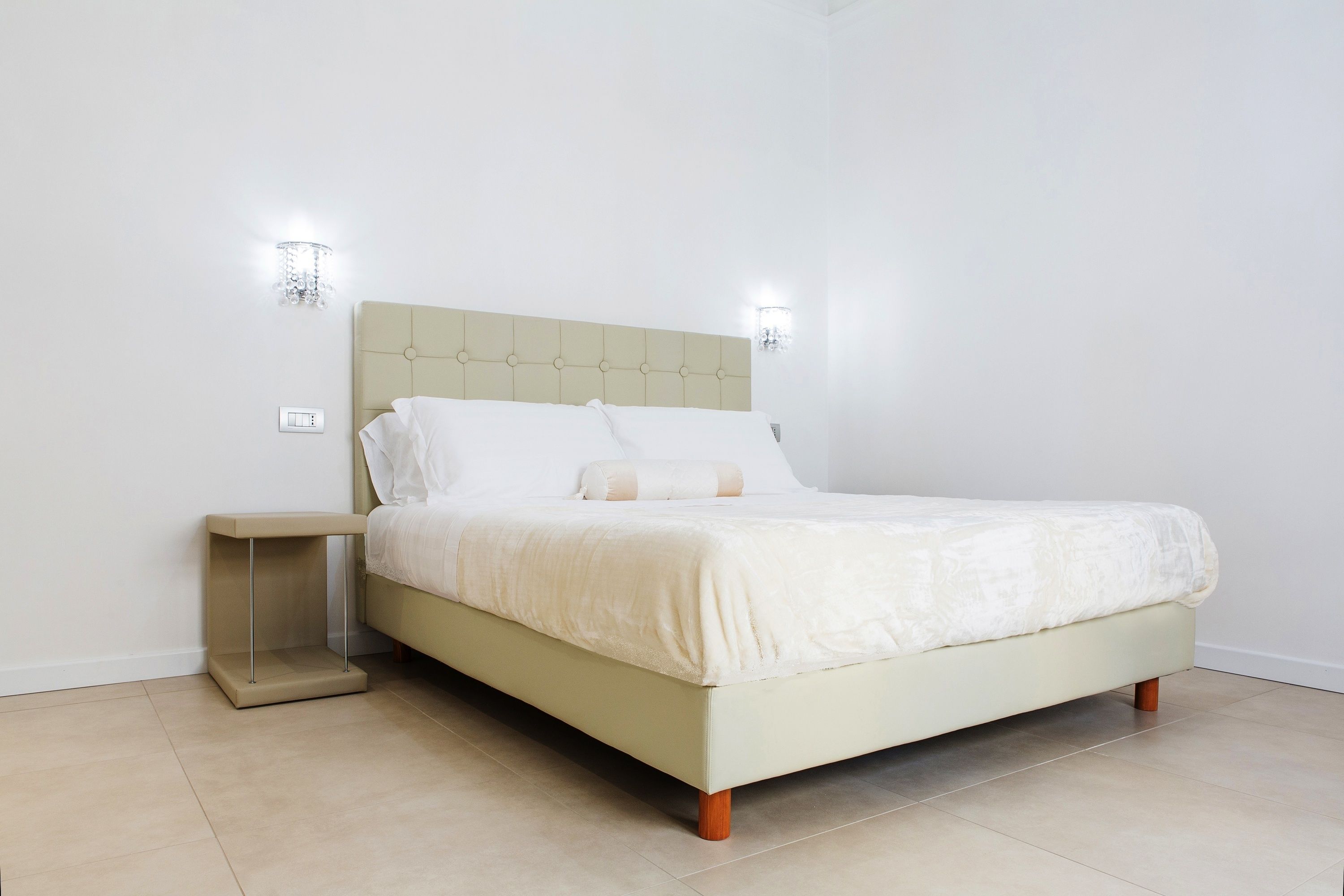 A bed with a beige headboard, white bedding, and two wall-mounted light fixtures.