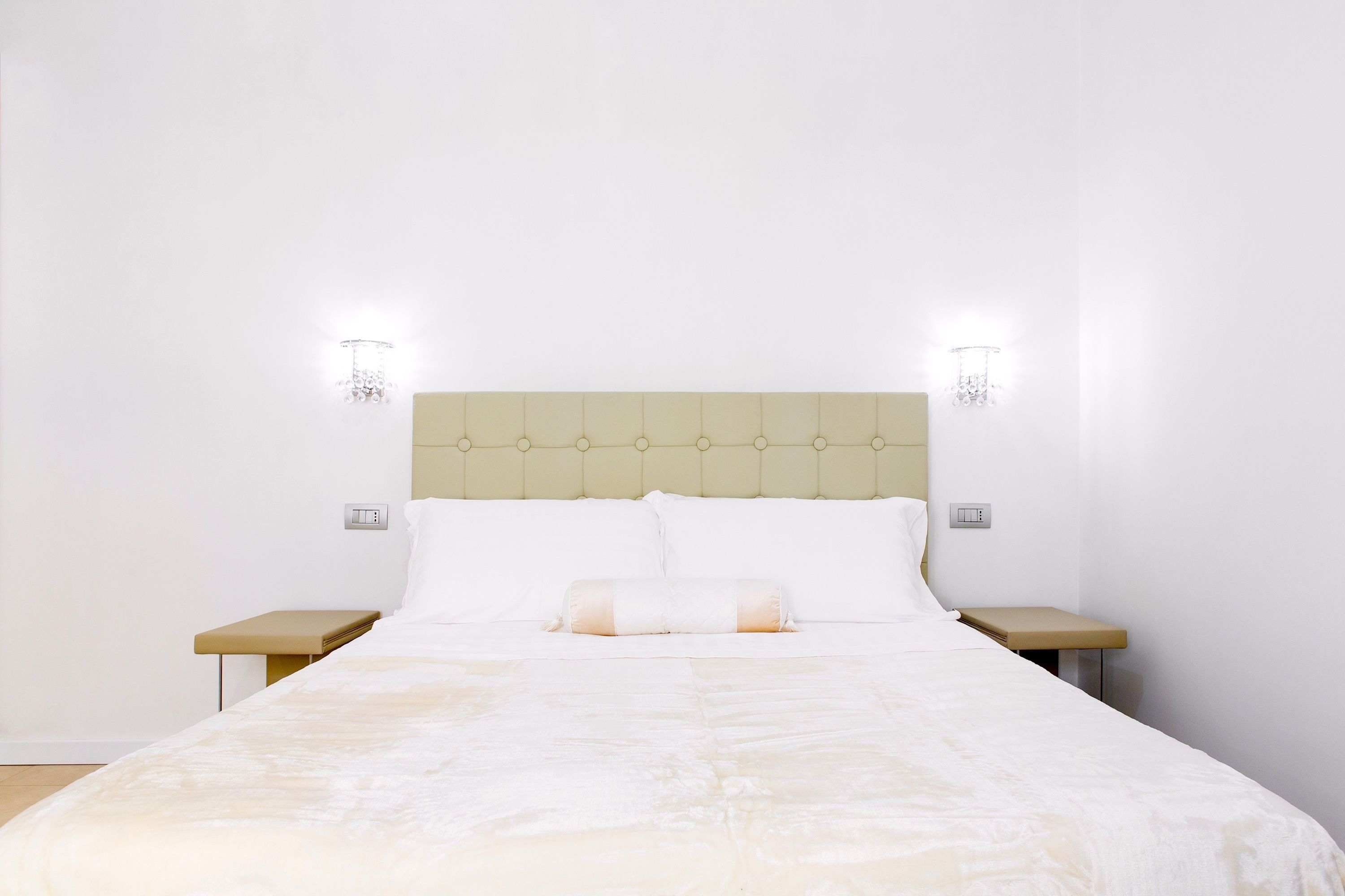 A neatly made bed with a beige headboard, two bedside tables, and wall-mounted lights.